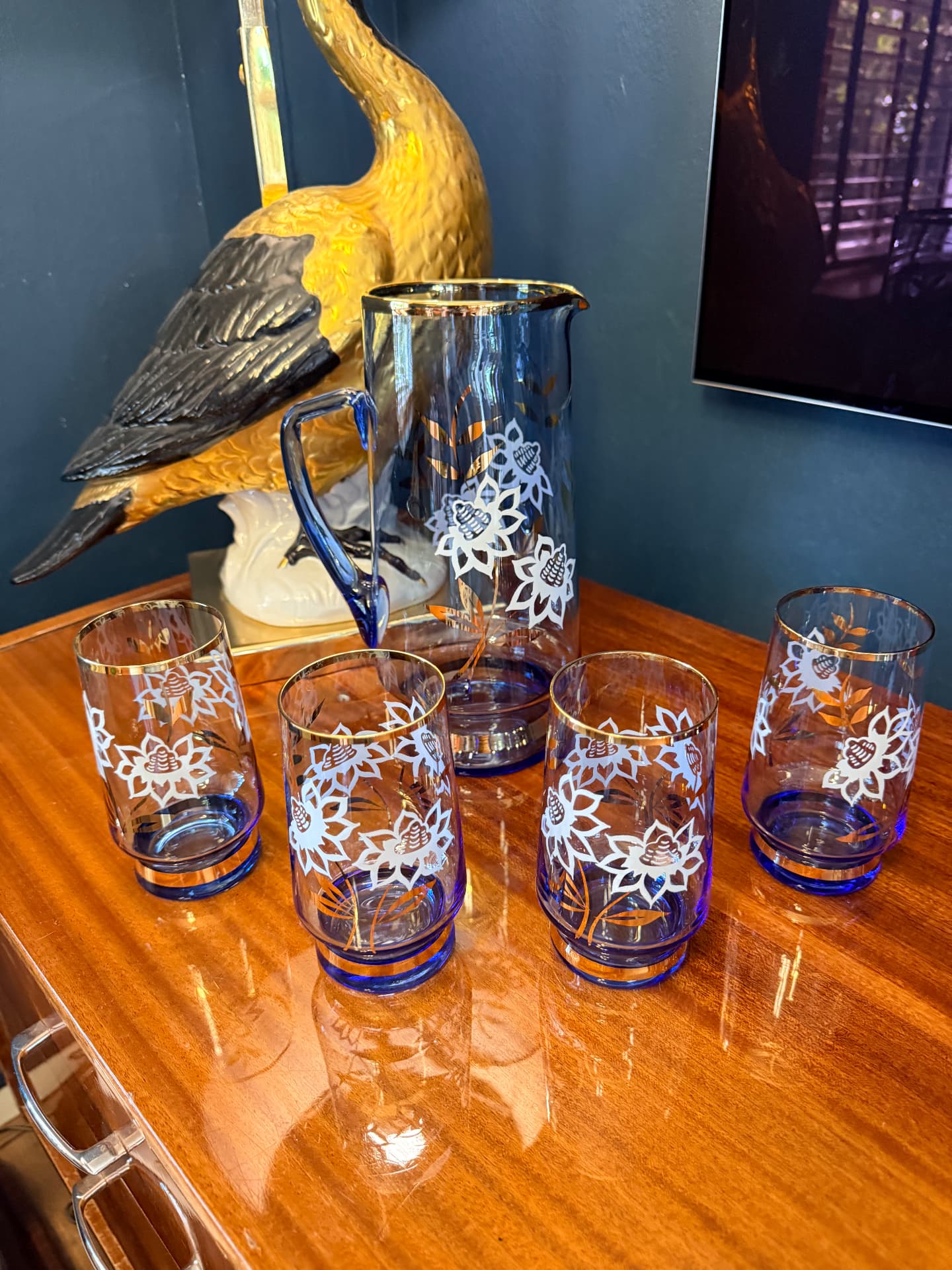 Vintage blauw glazen karaf met vier glazen met witte bloemen en gouden randen, voor een messing vogelbeeld