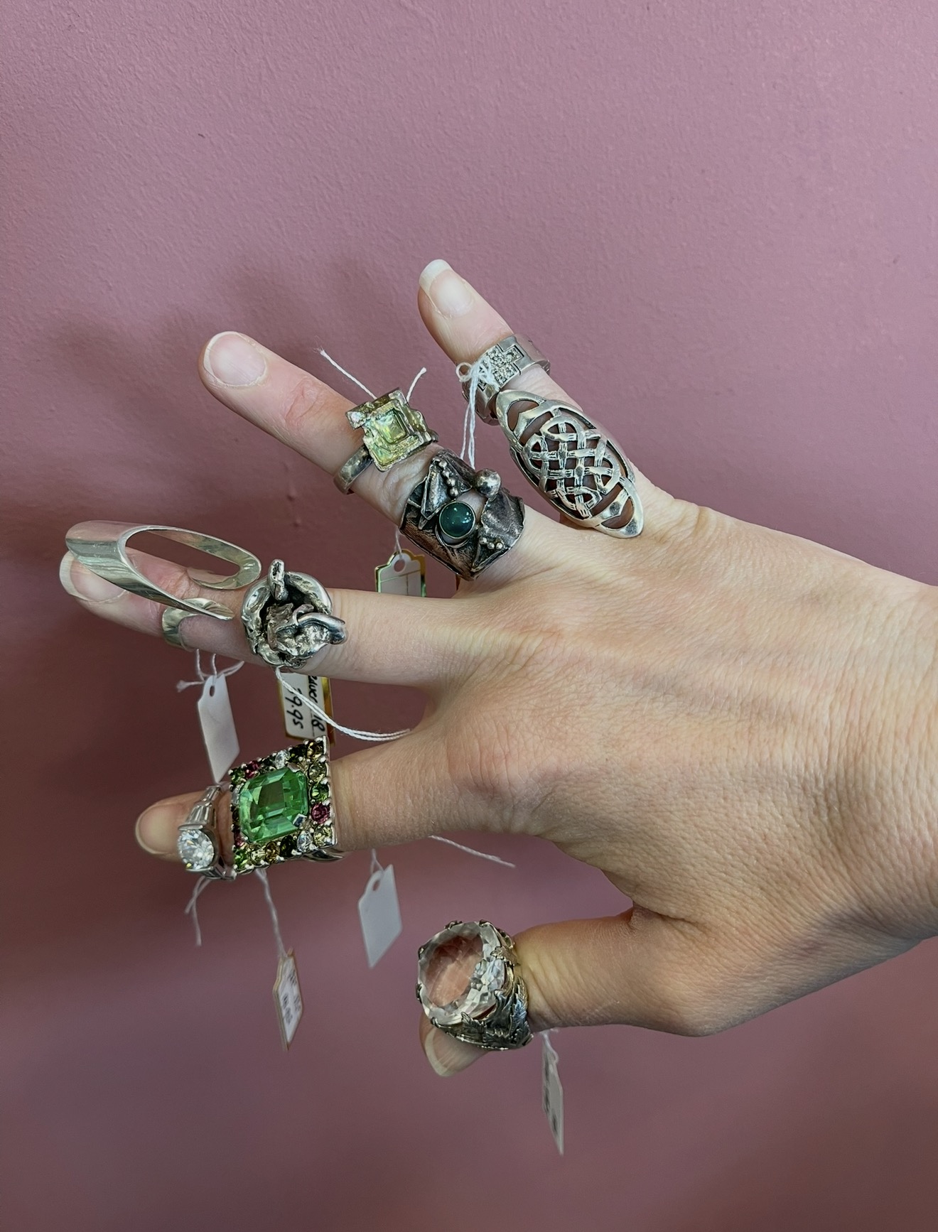 Hand met een collectie vintage zilveren ringen met groene stenen, knoopsgatenmotief en prijskaartjes
