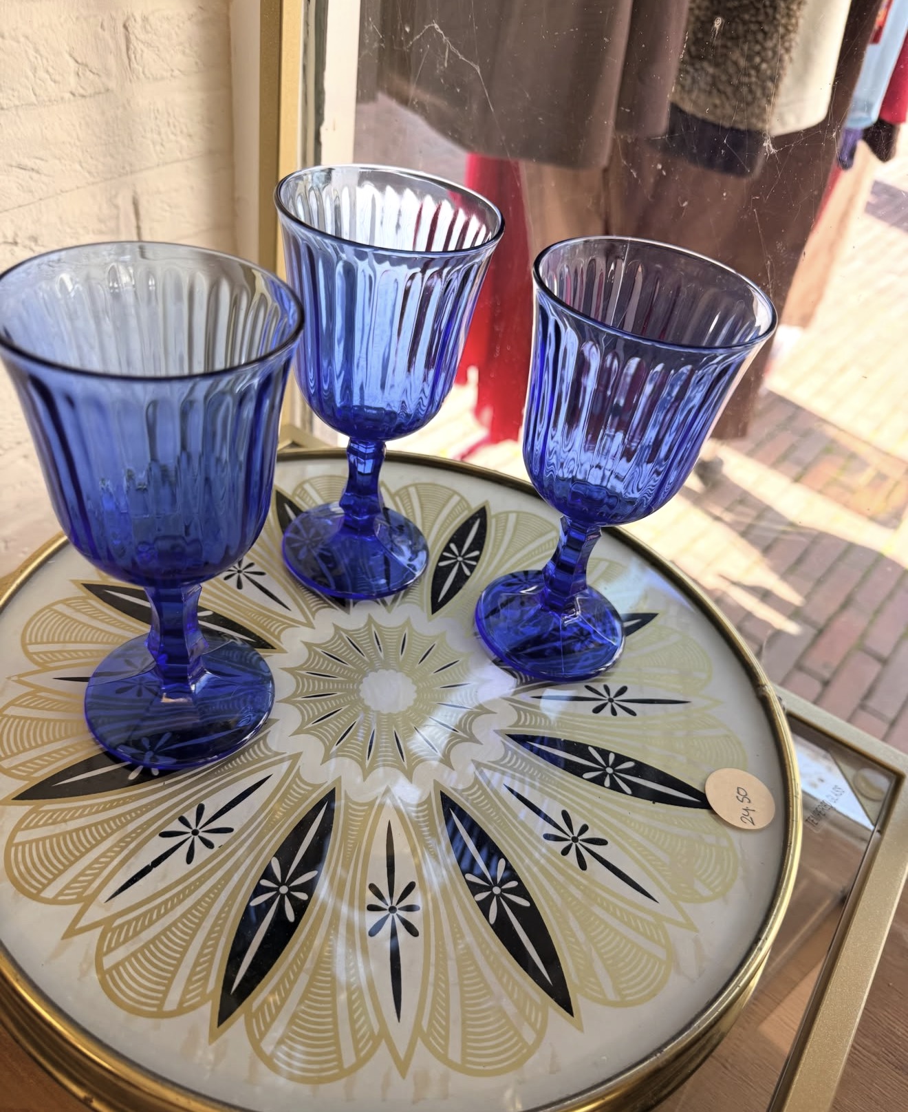 Drie kobaltblauwe vintage glazen op een ronde tafel met goudzwart retro dessin bij de etalage