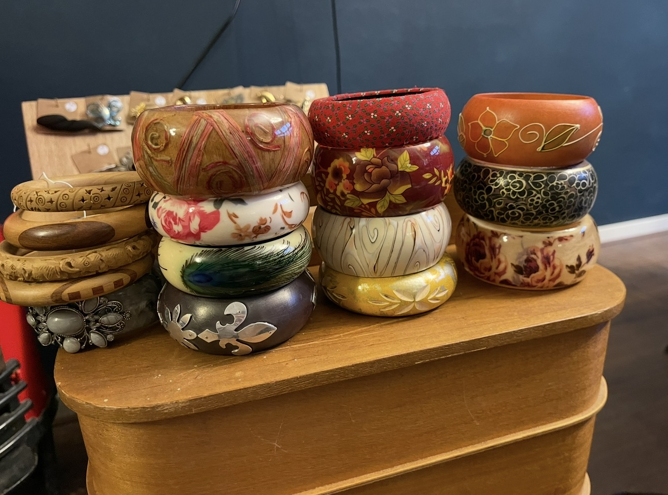 Stapels vintage armbanden in hout, beschilderd hout en stof met bloem- en pauwveermotieven op een houten kistje