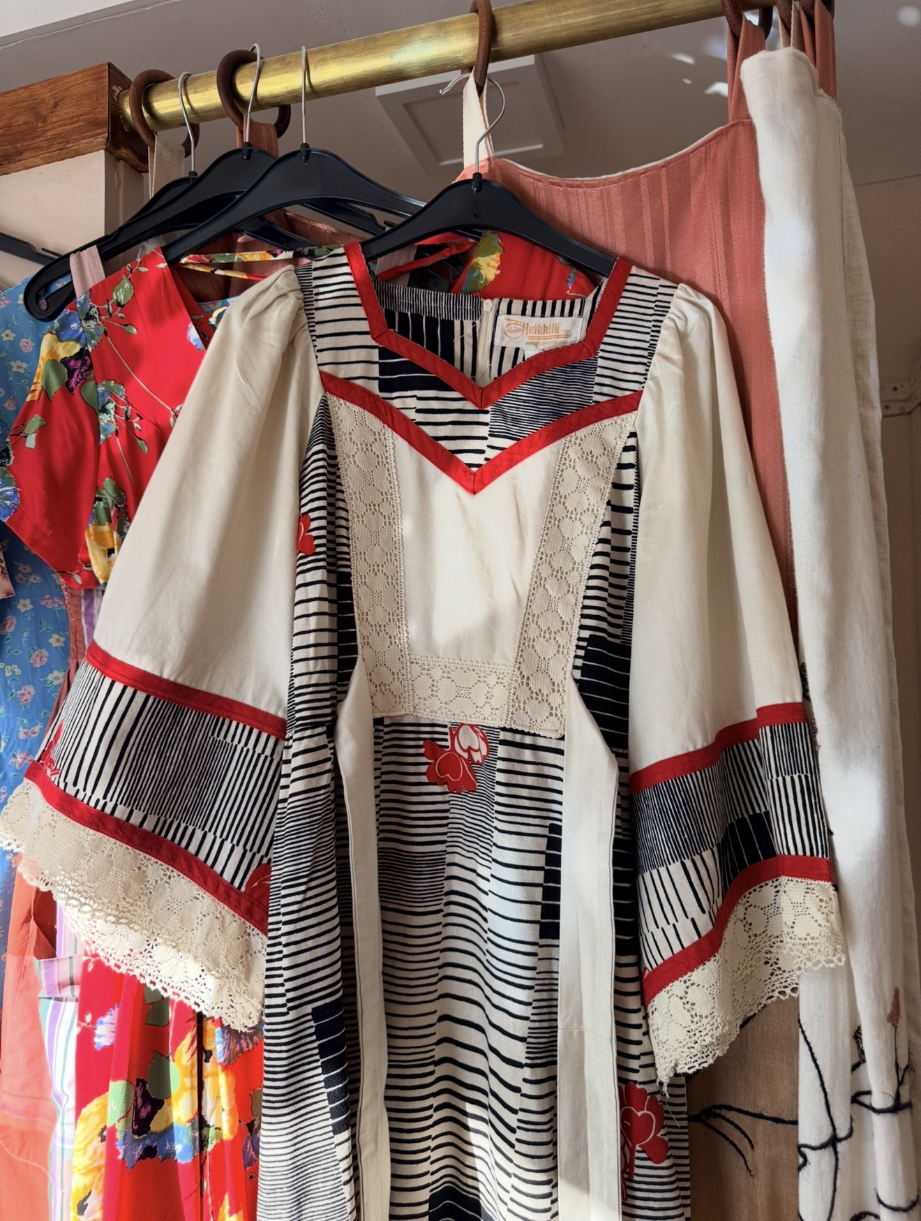 Vintage crème blouse met zwart-wit streepdessin en rode biezen aan een messing kledingroede