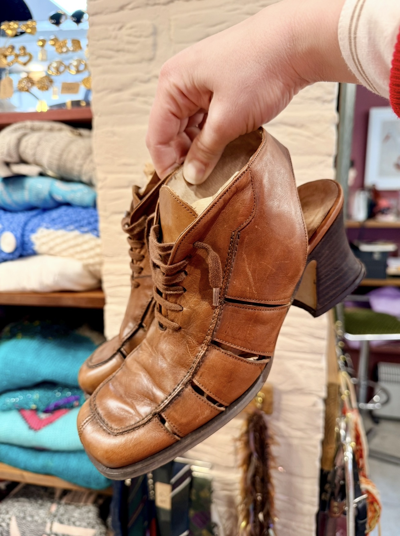 Cognac leren vintage schoenen met blokhak in de hand, voor schappen met gekleurde truien