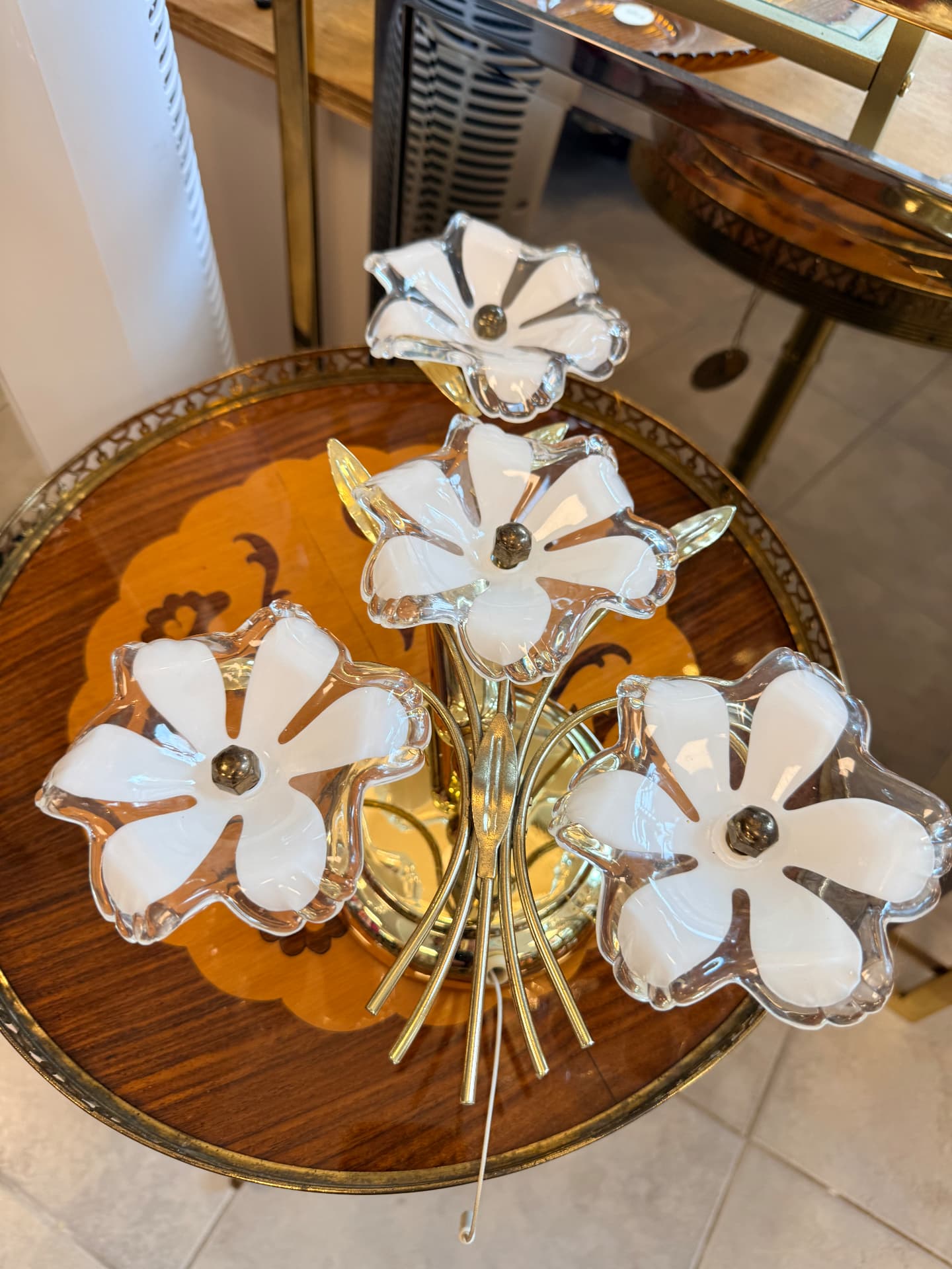 Vintage messing wandlamp met witte glazen bloemen op een messing bijzettafel