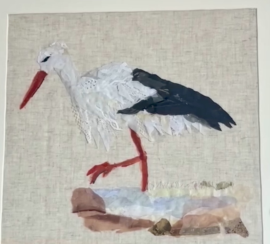 Textielkunst van een ooievaar, gemaakt van oude kledingstukken, kant en labels op linnen