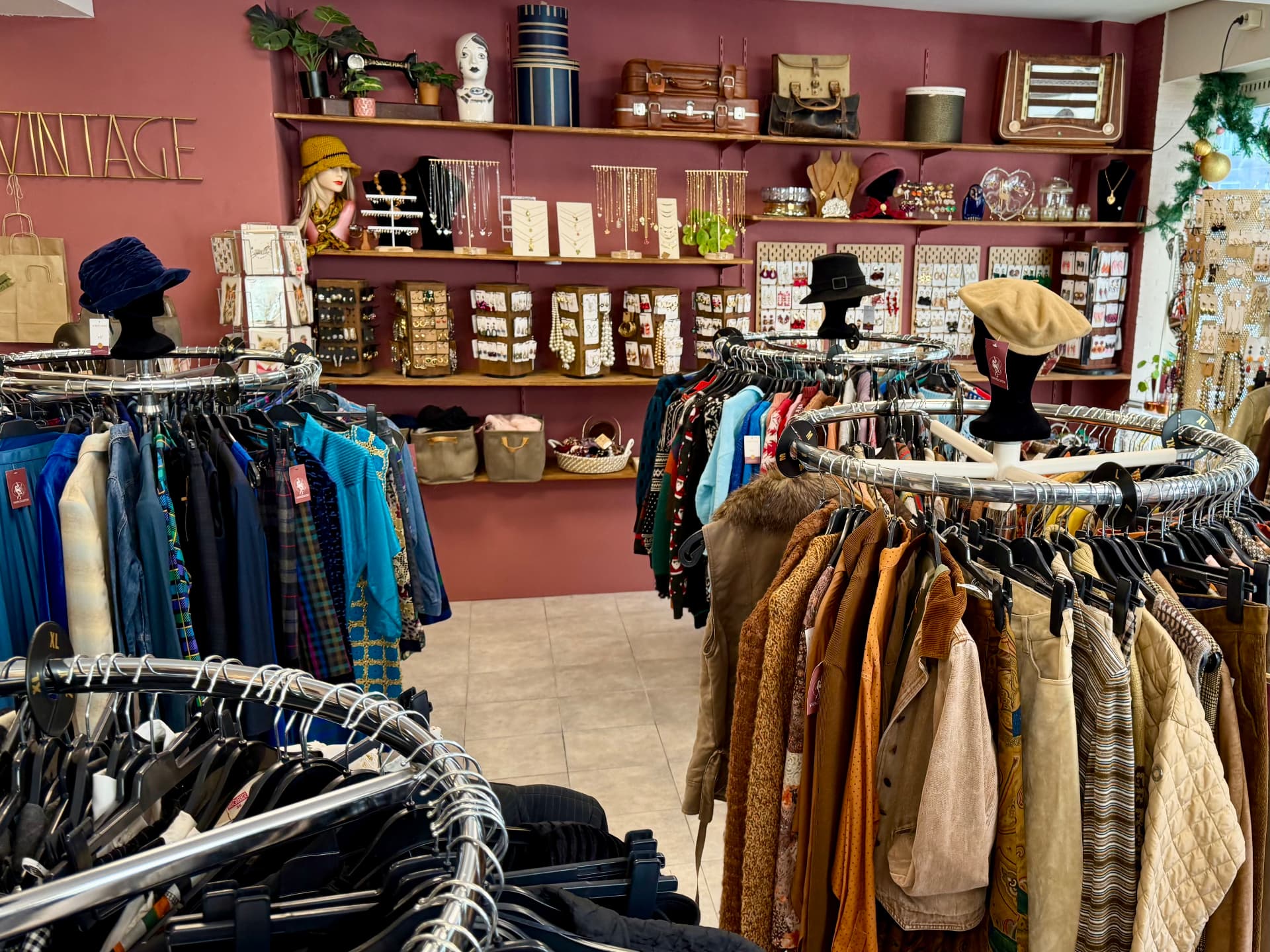 Wijd interieur van VintageGlitch met ronden rekken vintage kleding, hoeden op bokken en een bordeauxrode wand vol sieraden