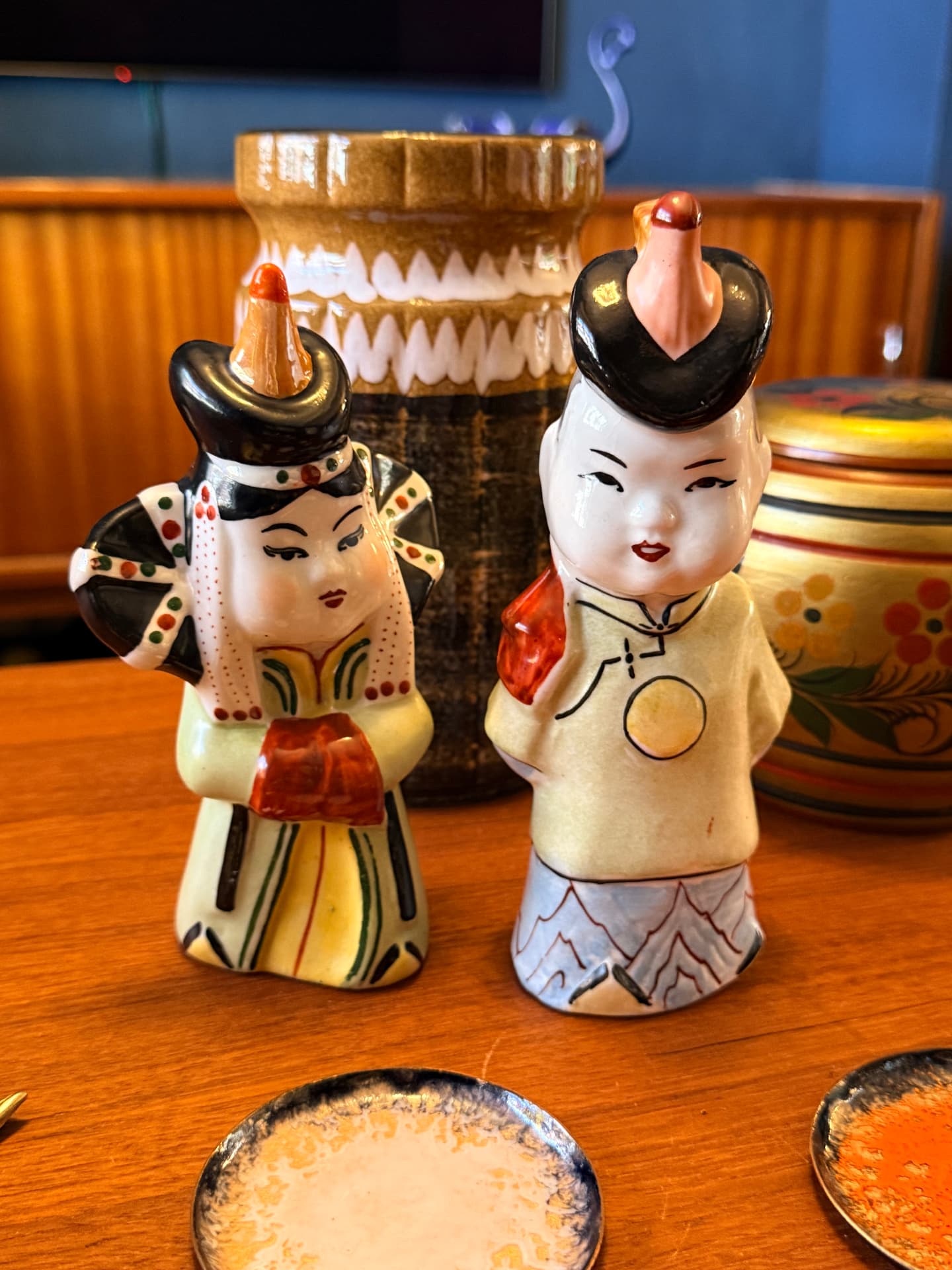 Twee vintage keramische figuurtjes in traditionele kleding naast een West-German vaas op een teakhouten tafel