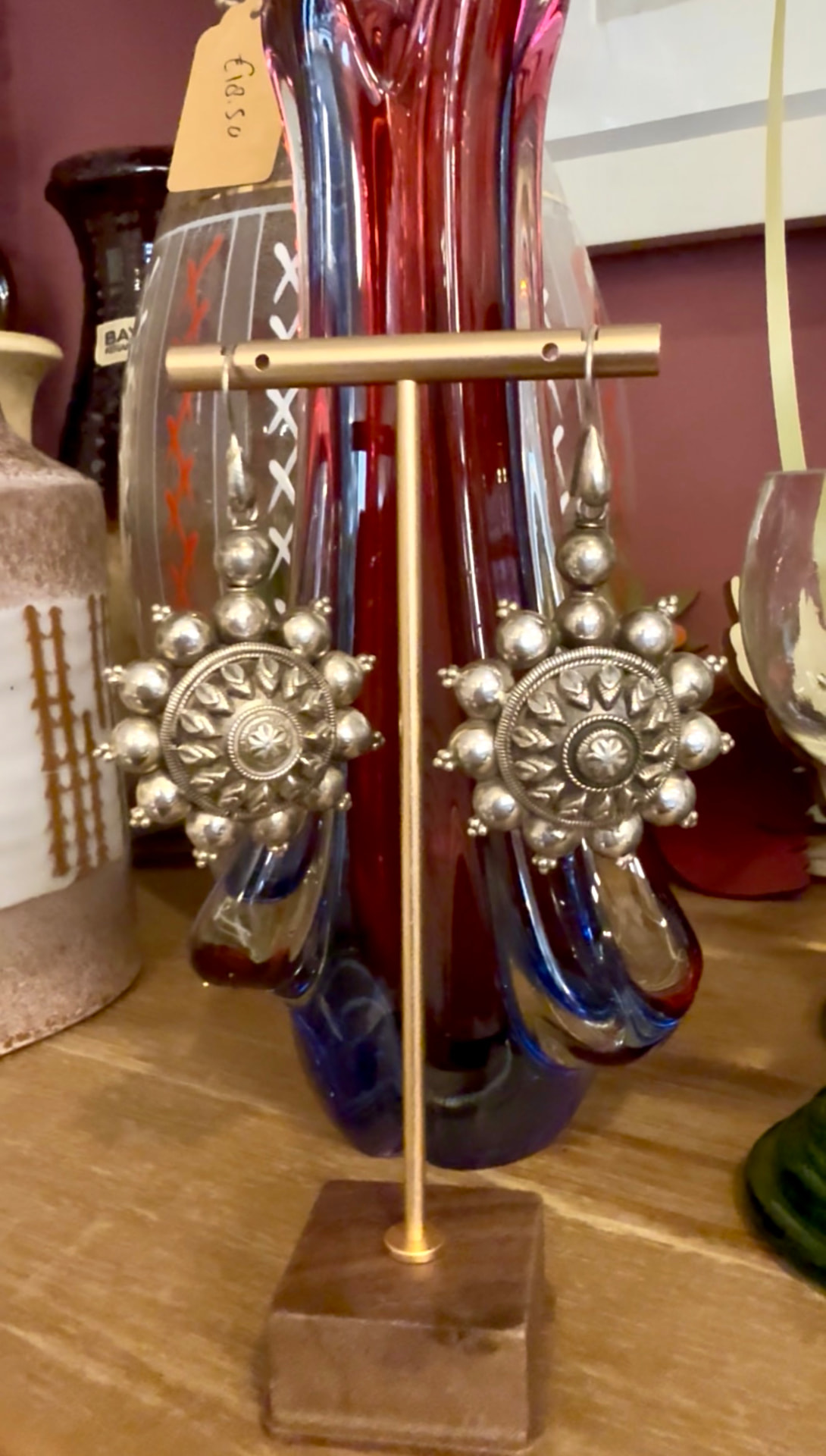 Grote zilveren vintage oorbellen met bolletjes en bloemmotief aan een messing standaard voor een rood glazen vaas