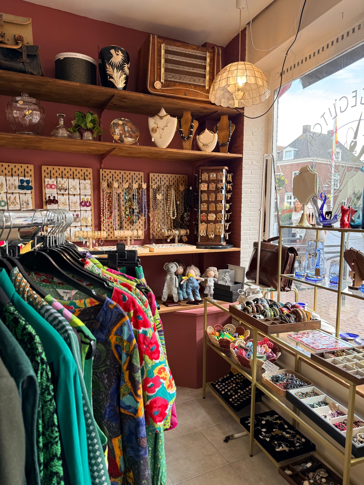 De sieradenhoek van VintageGlitch met houten schappen vol kettingen en oorbellen, een vintage radio en bloemlamp bij het etalageraam