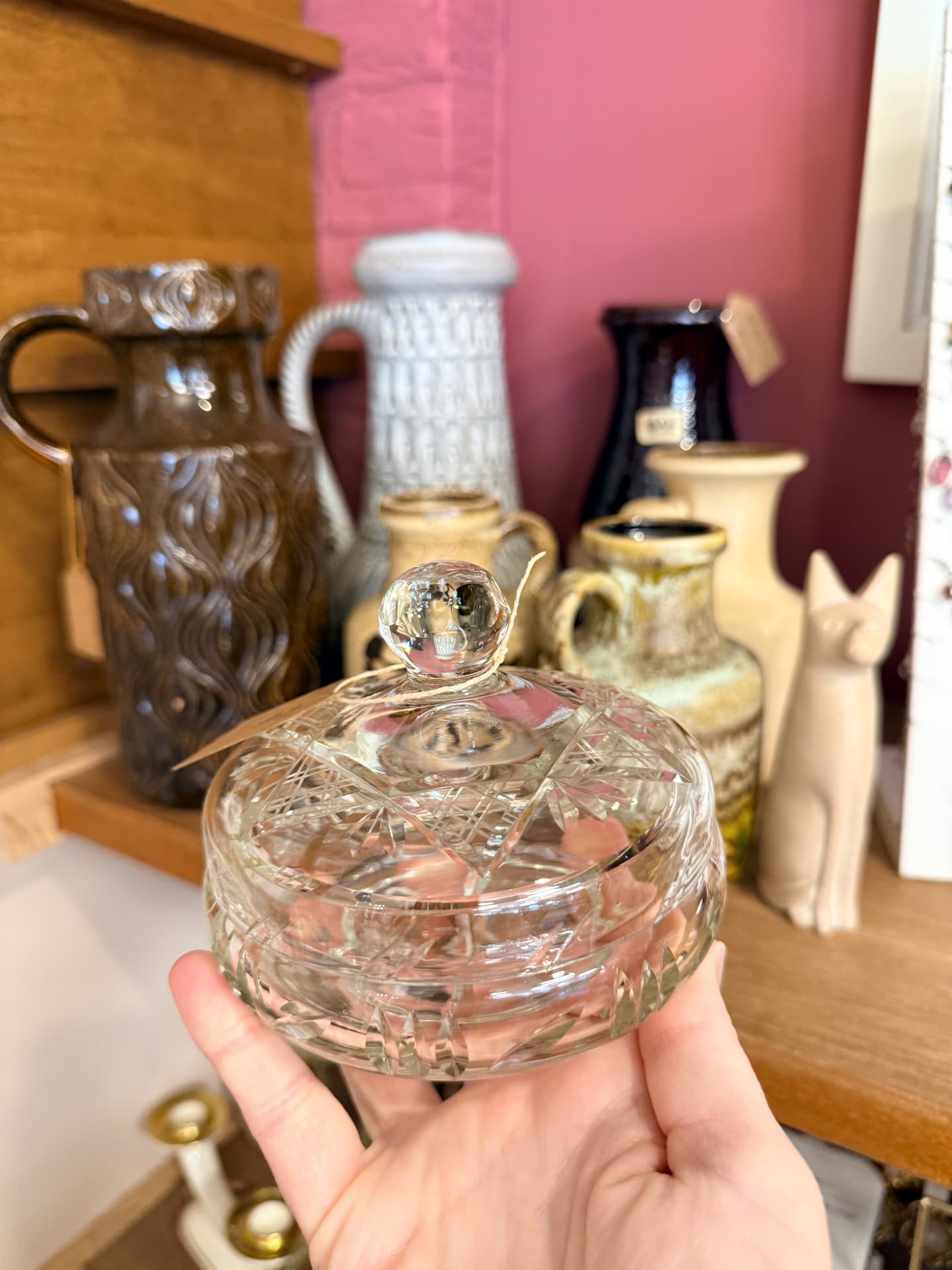 Kristallen bonbonnière in de hand voor een schap met vintage West-German vazen tegen een oudroze wand